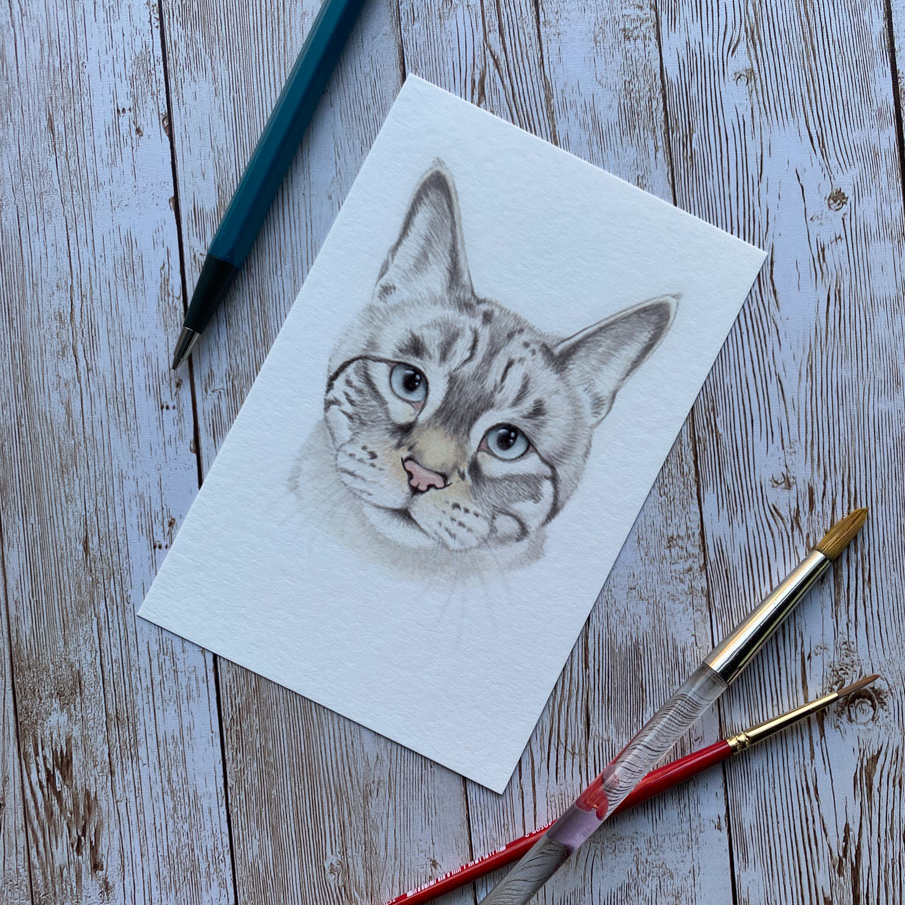 Cat drawing on paper with art supplies on a wooden surface