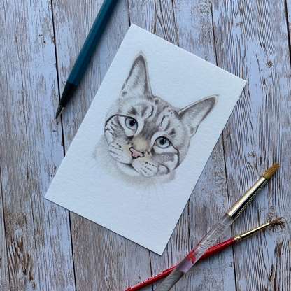 Cat drawing on paper with art supplies on a wooden surface