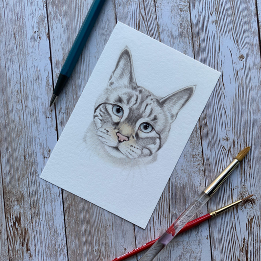 Cat drawing on paper with art supplies on a wooden surface